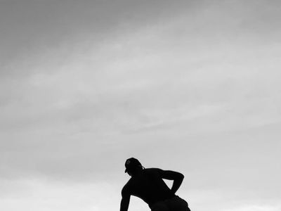 Silhouetted figure in a stretching pose against sunset.